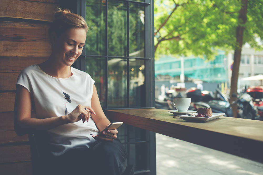 woman with beautiful smile reading good news on mobile phone during rest in coffee shop